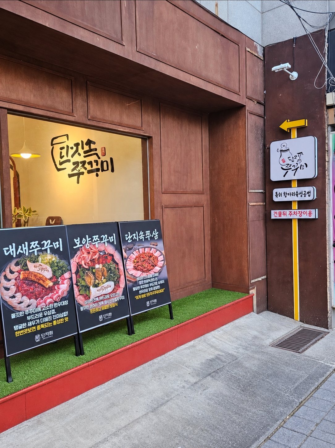 입구 앞 메뉴 입간판 세 개와 붓글씨 로고 창, 노란 화살표 표지판